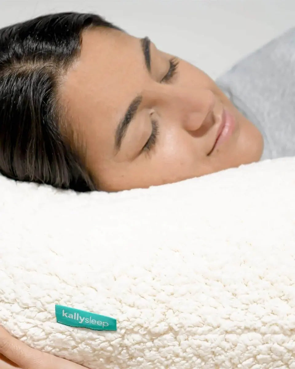 Woman resting on a soft white fleece pillow with eyes closed, close-up, kallysleep label visible
