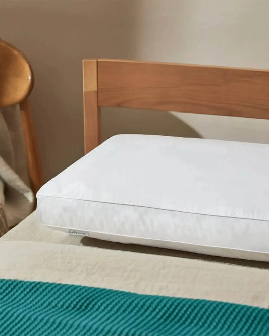 White ergonomic pillow on bed with teal blanket and wooden chair in bedroom