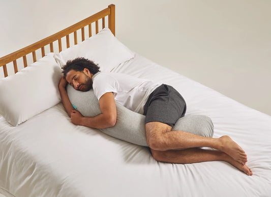 Man sleeping on a bed with a kallysleep body pillow