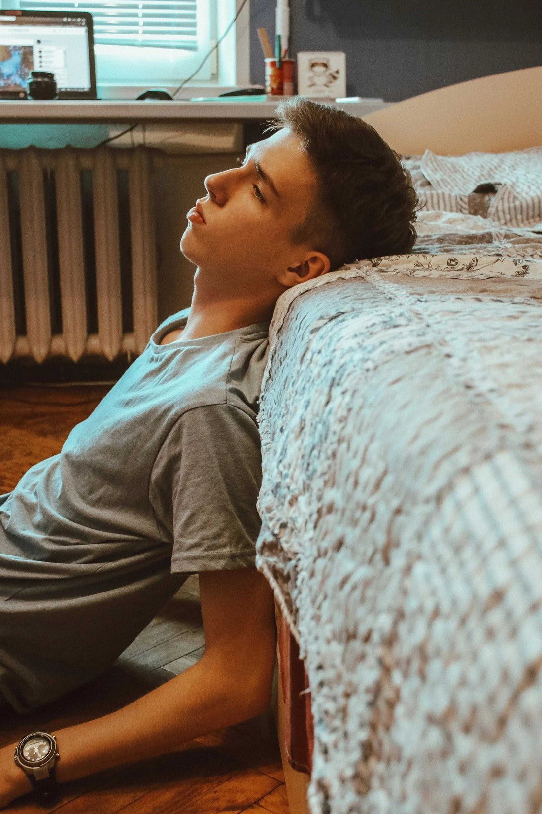 Young man sitting on floor near bed contemplating exercise before bed and its impact on sleep