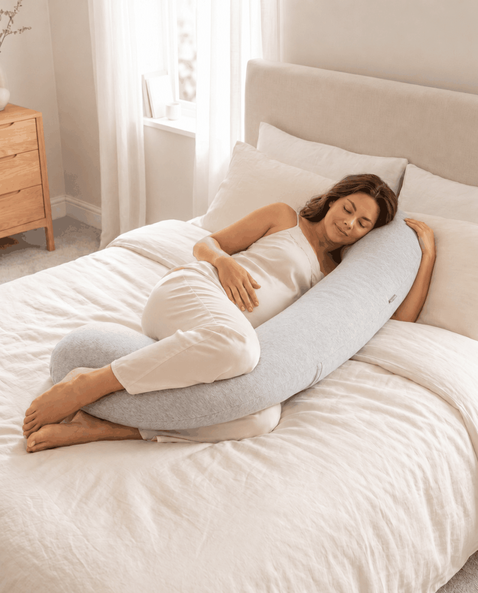 Woman lying on a bed using an U-shaped body pillow in a bedroom setting.